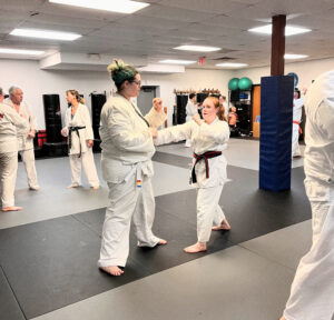 Two women practicing partner techniques during a group adult karate class, benefiting from shared learning, teamwork, and real-time feedback in a supportive training environment.